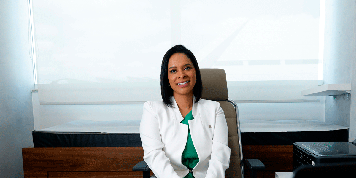 Dra. Lourena Lima sentada em seu consultório, de jaleco branco, sorrindo